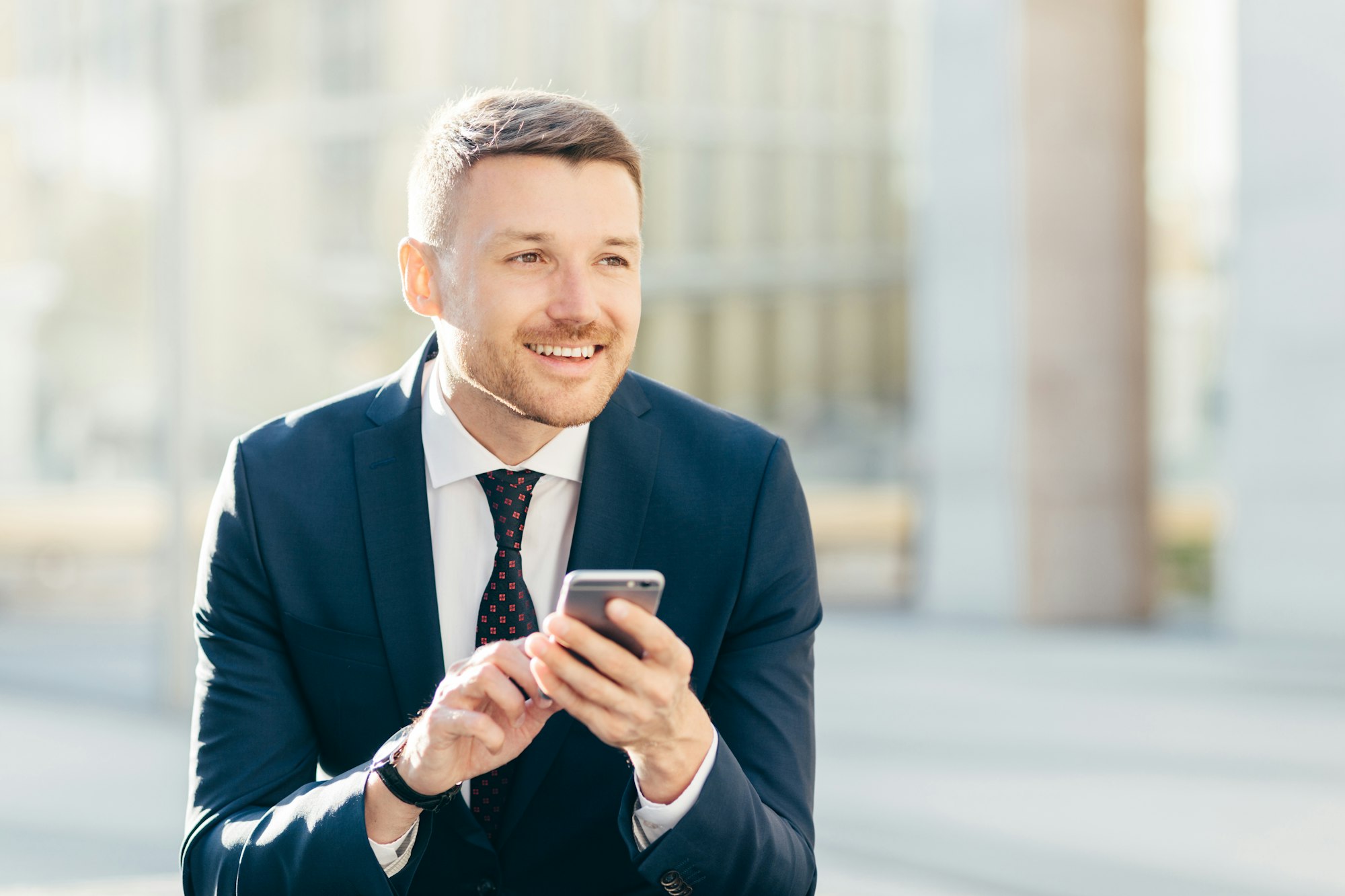 Delighted thoughtful elegant male marketing trader in formal black suit, uses modern cell phone